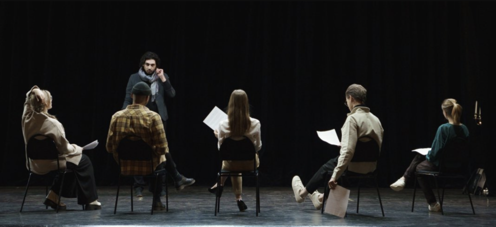 A theatre professor talking to a class of theatre students on stage